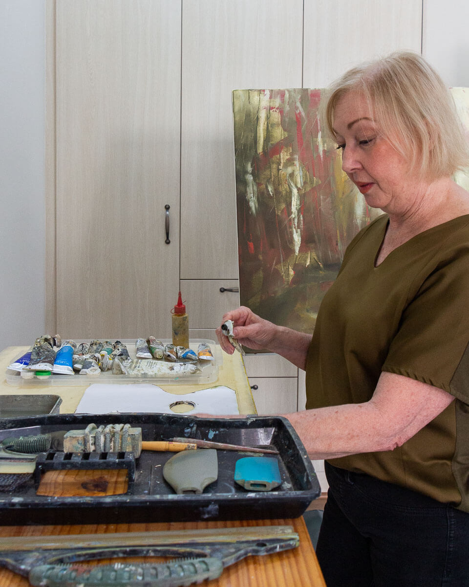 Janet Dirksen mixing paints in her art studio, next to a painting in progress.